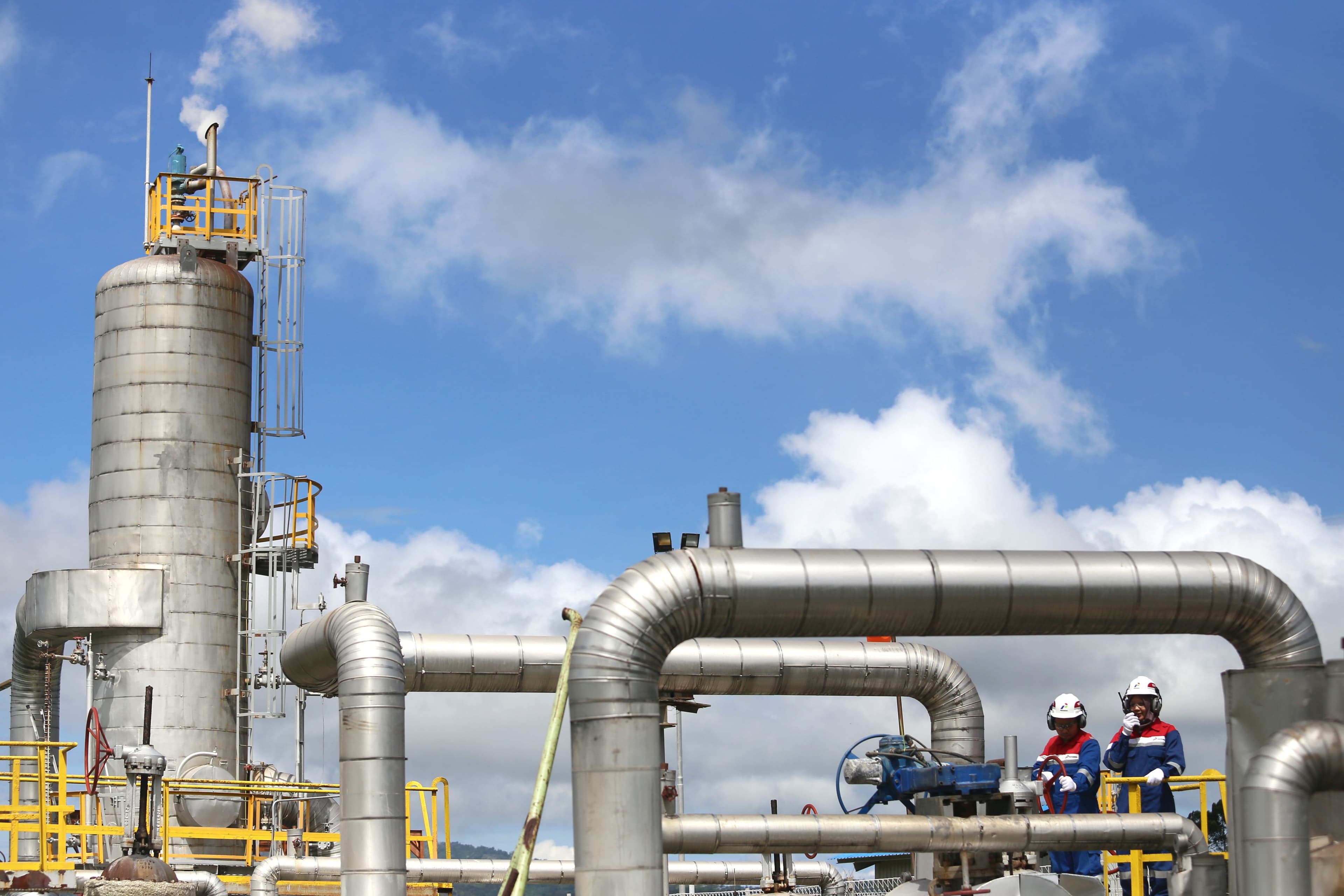 Refinery columns and pipework, with two workers in protective coveralls and hard hats